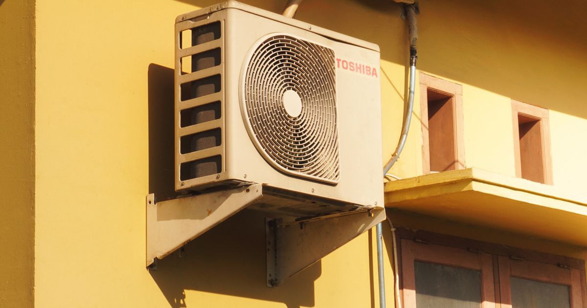 The outdoor unit of a split aircon mounted on a yellow wall