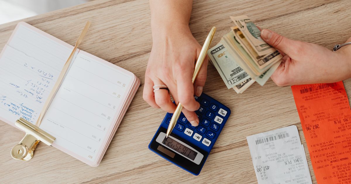 Hands working out a sum on a blue calculator next to banknotes and till slips