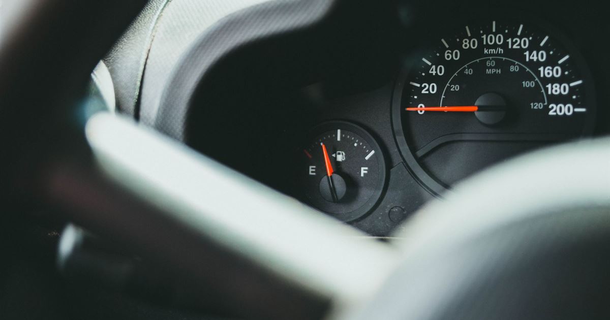 Car dashboard with the fuel gauge needle close to empty beside the speedometer