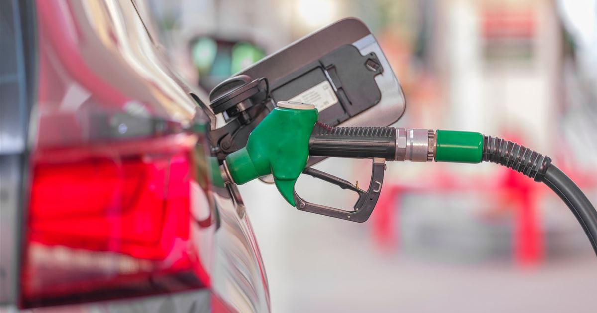 Green petrol nozzle in the open fuel flap of a silver car at a filling station