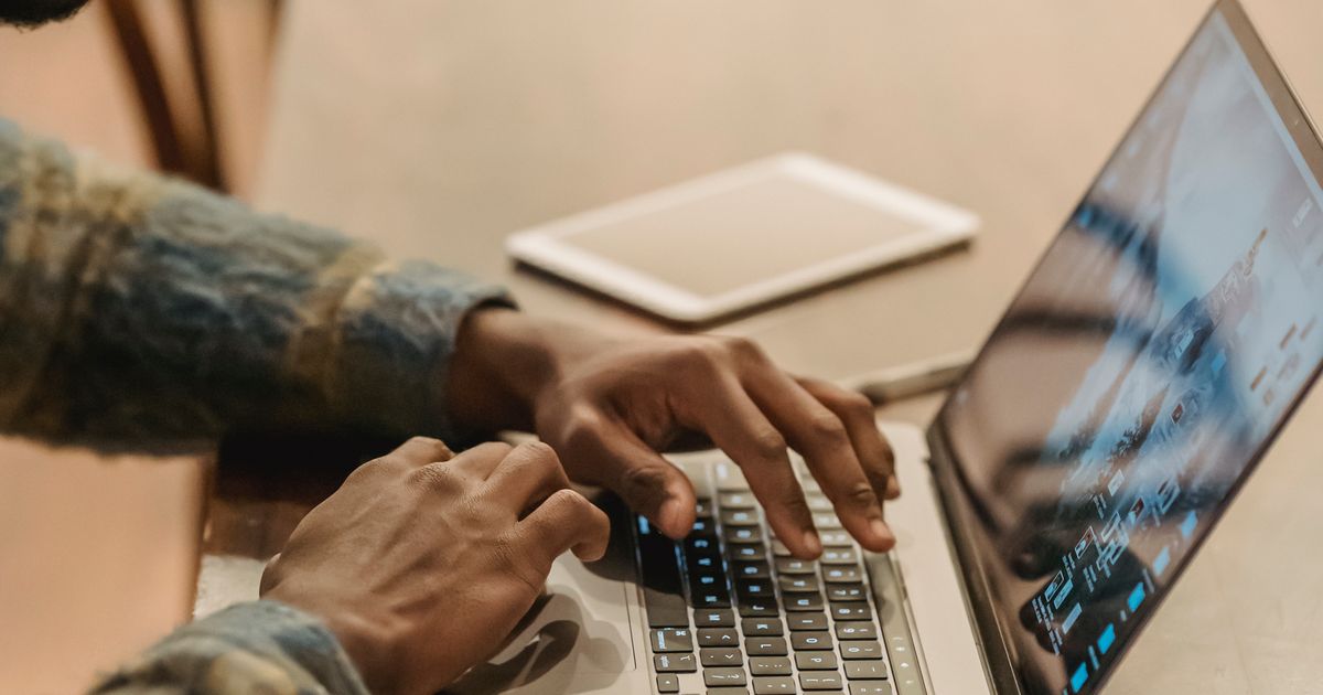 Hands typing on a laptop on a wooden table, a tablet beside it