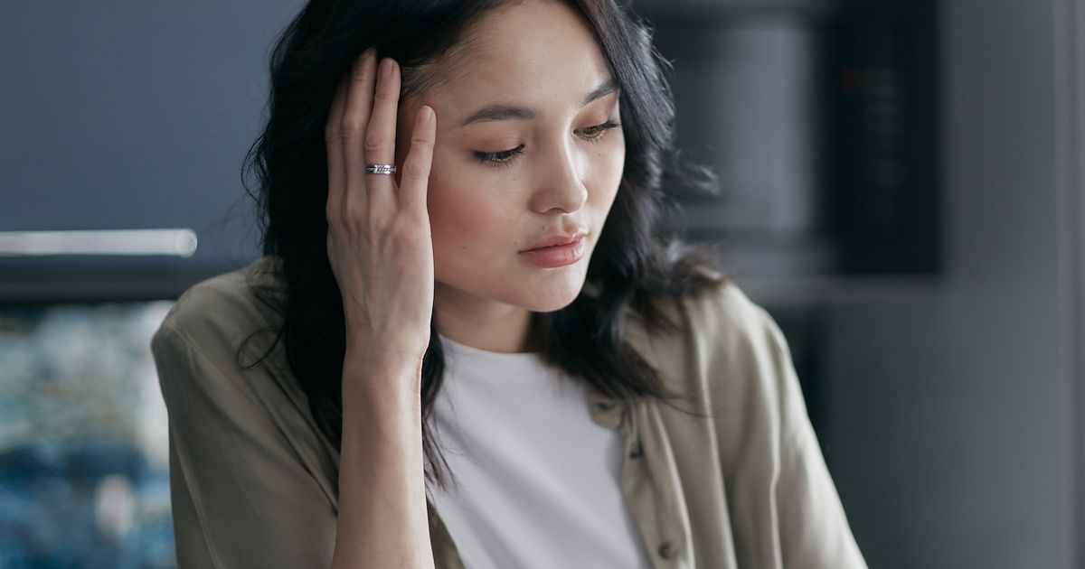 A worried woman with her hand to her head, deep in thought