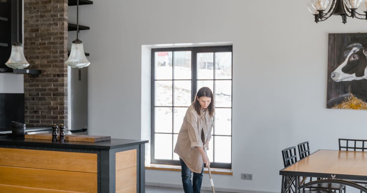 A woman mopping the floor of a bright open-plan kitchen and dining room