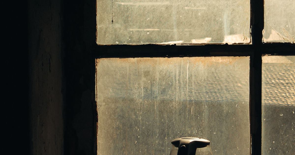 A vintage electric kettle on a dusty windowsill, backlit by soft daylight