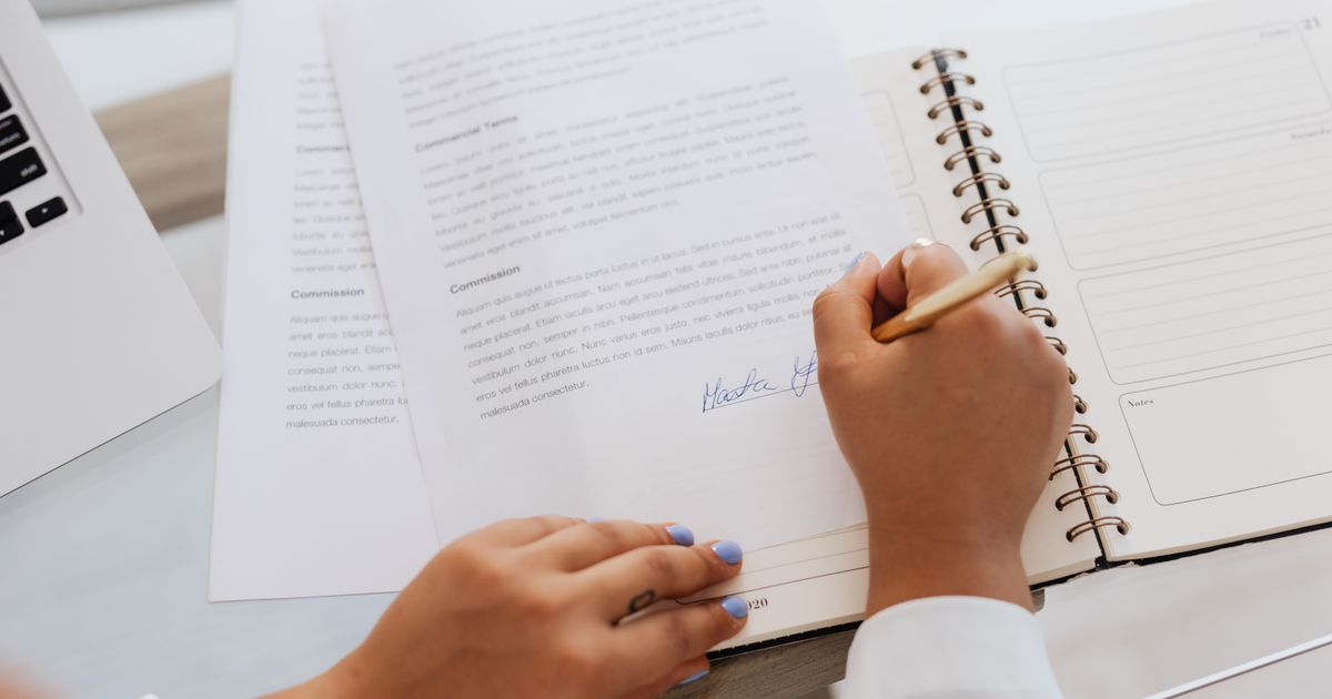 Close-up of hands signing a contract on a desk beside office supplies