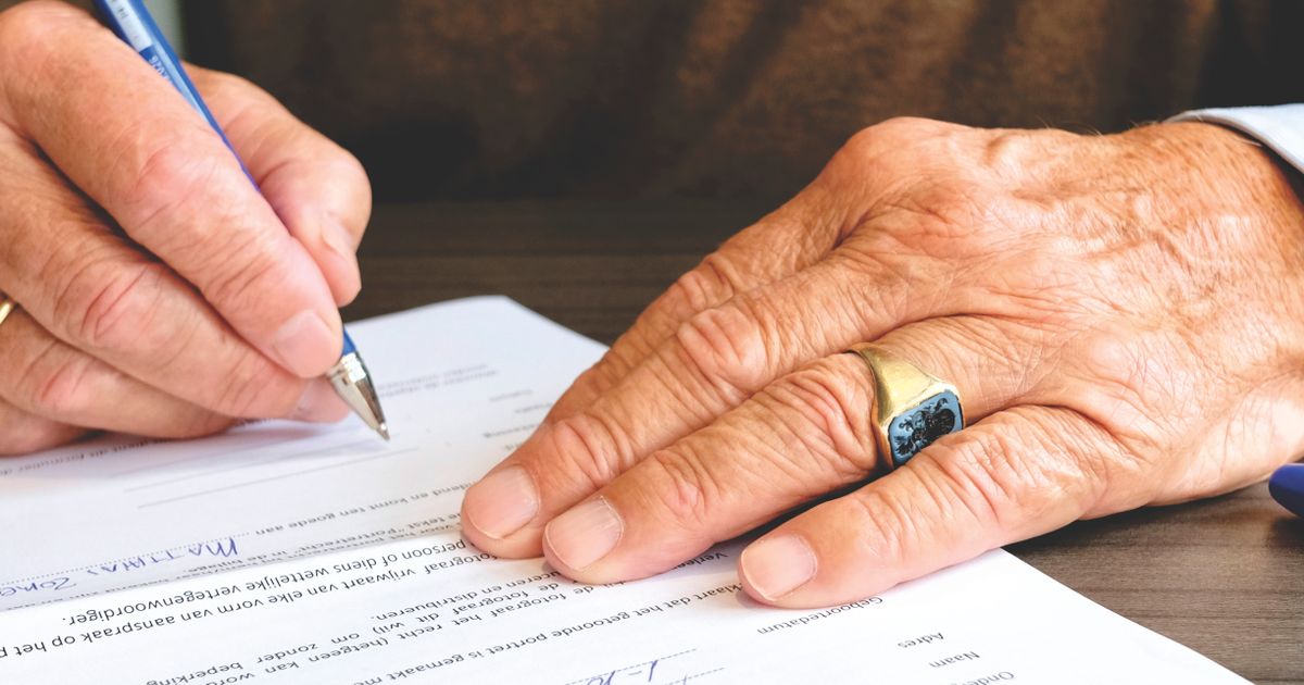 Close-up of an older person's hand with a gold ring signing a legal document