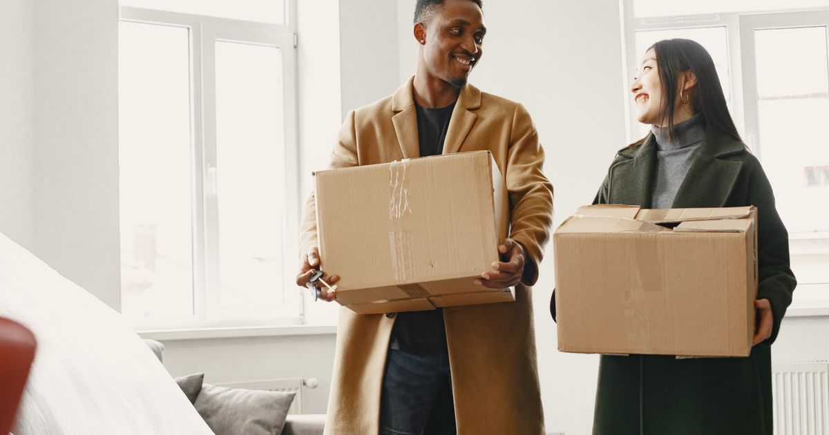 A smiling couple carrying moving boxes into their new home