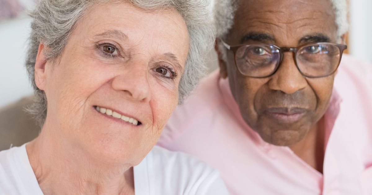 An older woman with grey hair and an older man in glasses sitting close together and smiling