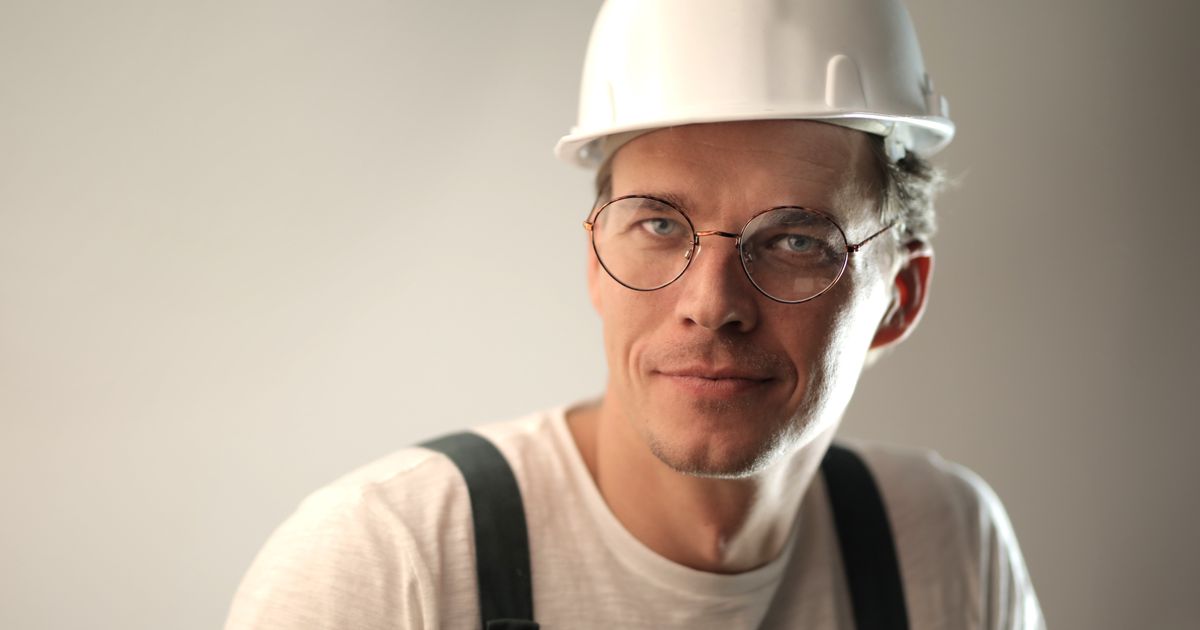 A smiling man in a white construction hard hat and safety glasses