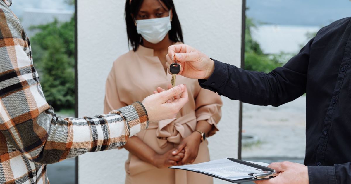 An agent hands a house key across to a buyer while holding a clipboard with the sale papers