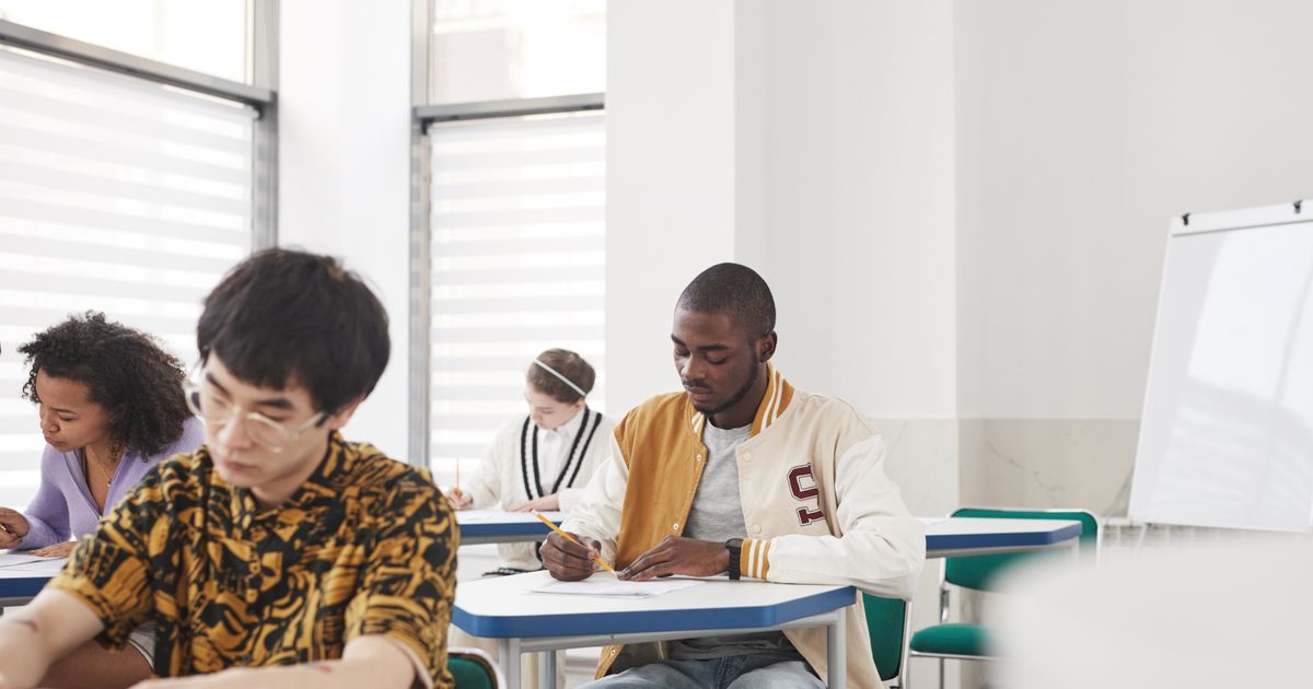 Students at their desks in a classroom, heads down, writing an exam