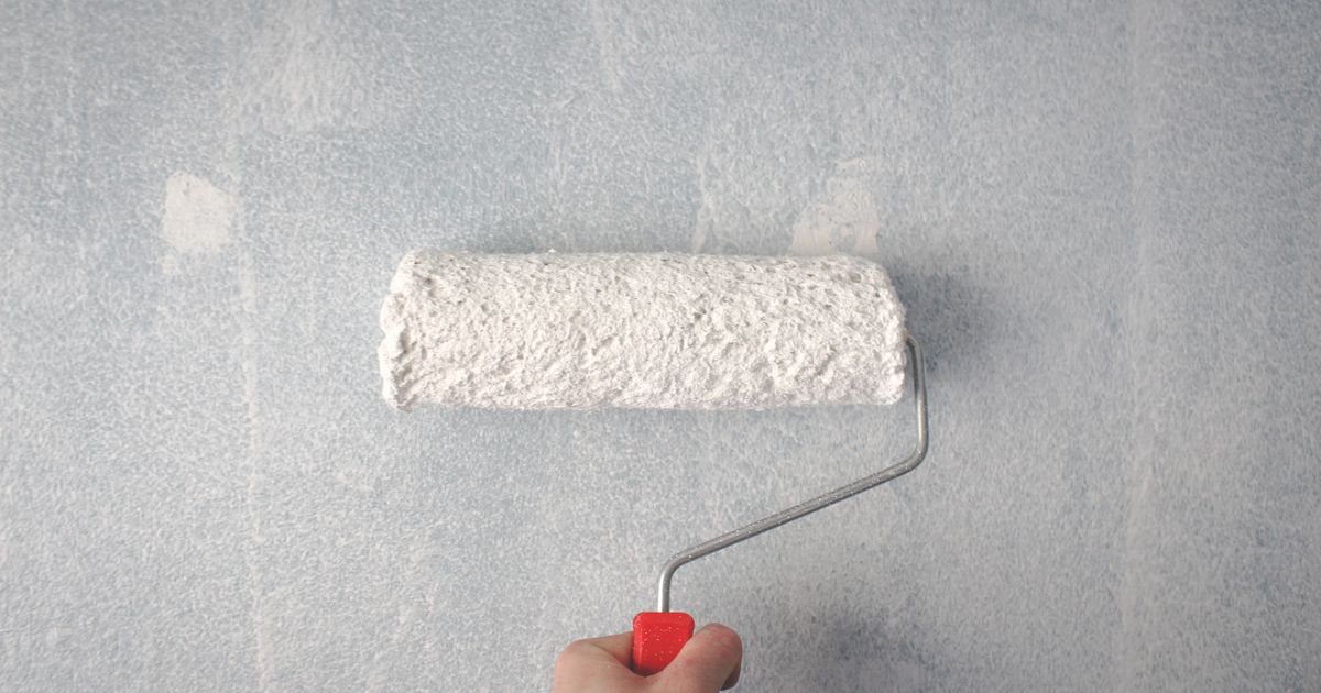 A hand rolling white paint onto a wall with a paint roller