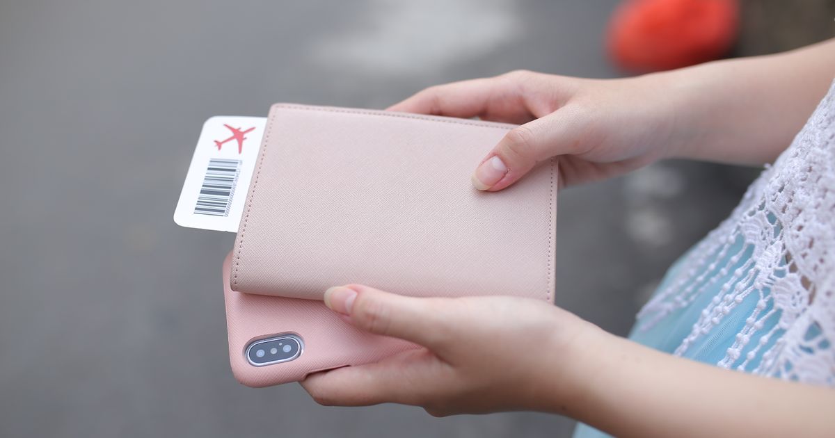 Hands holding a pink passport cover with a boarding pass and a phone
