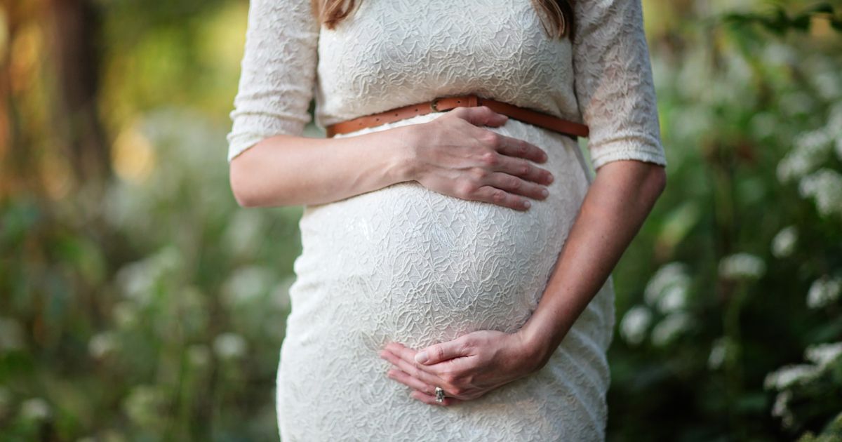A pregnant woman in a lace dress cradling her belly outdoors