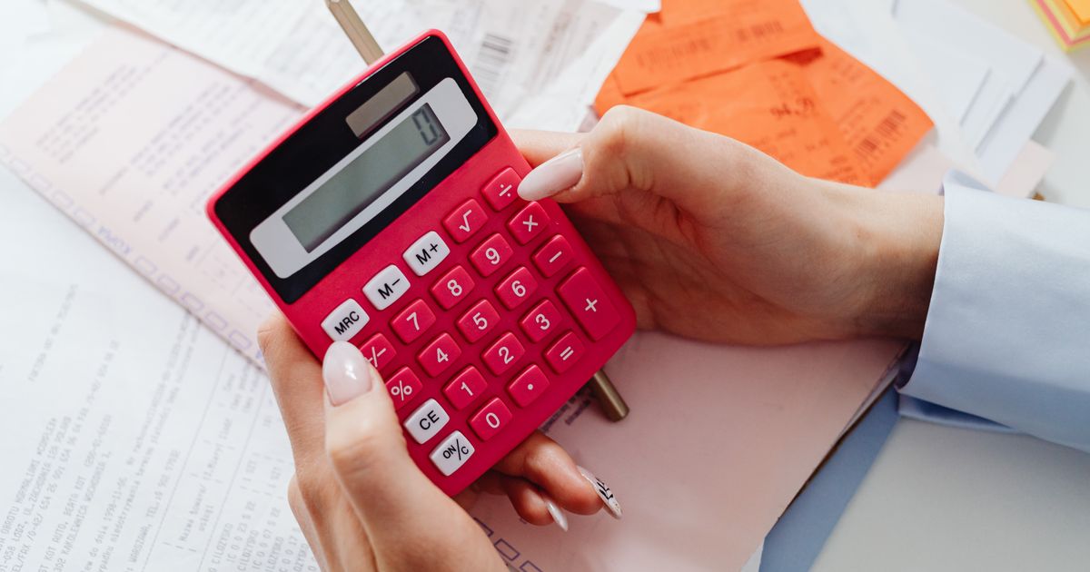 Close-up of hands holding a pink calculator over invoices and receipts