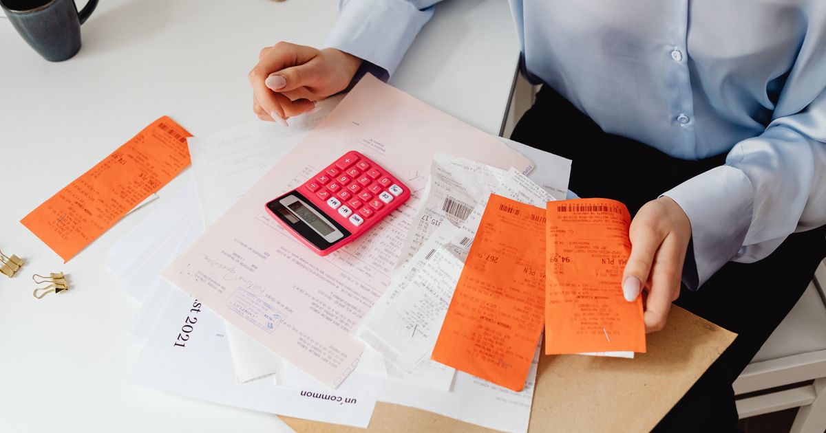 A woman sorting till slips beside a pink calculator and invoices on a desk