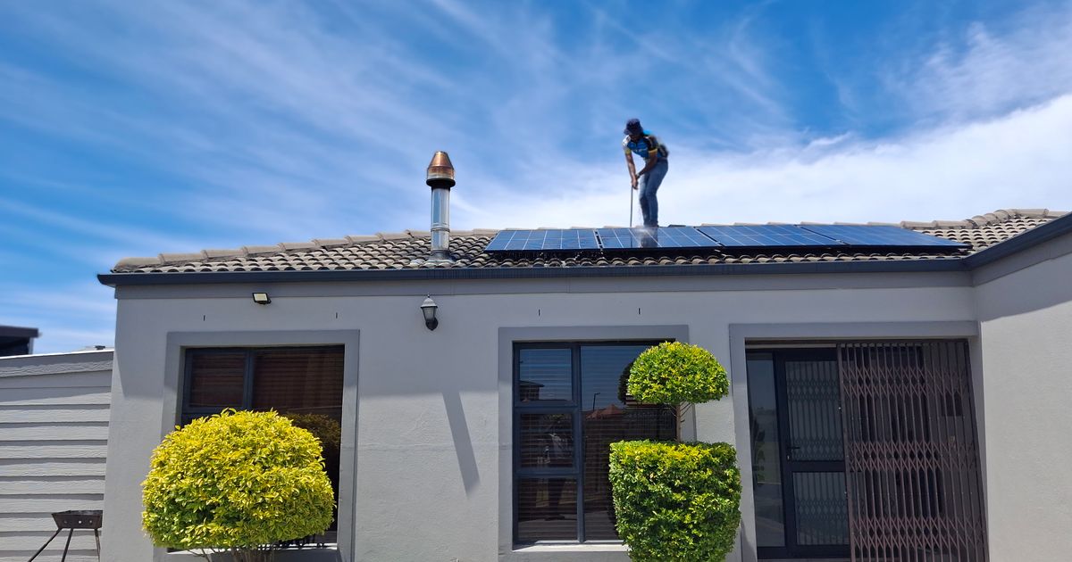 A worker cleaning solar panels on the tiled roof of a single-storey South African house