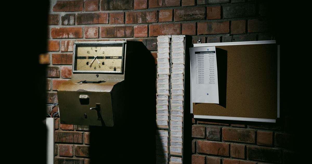 An old time clock and a rack of punch cards on a brick wall at a factory entrance